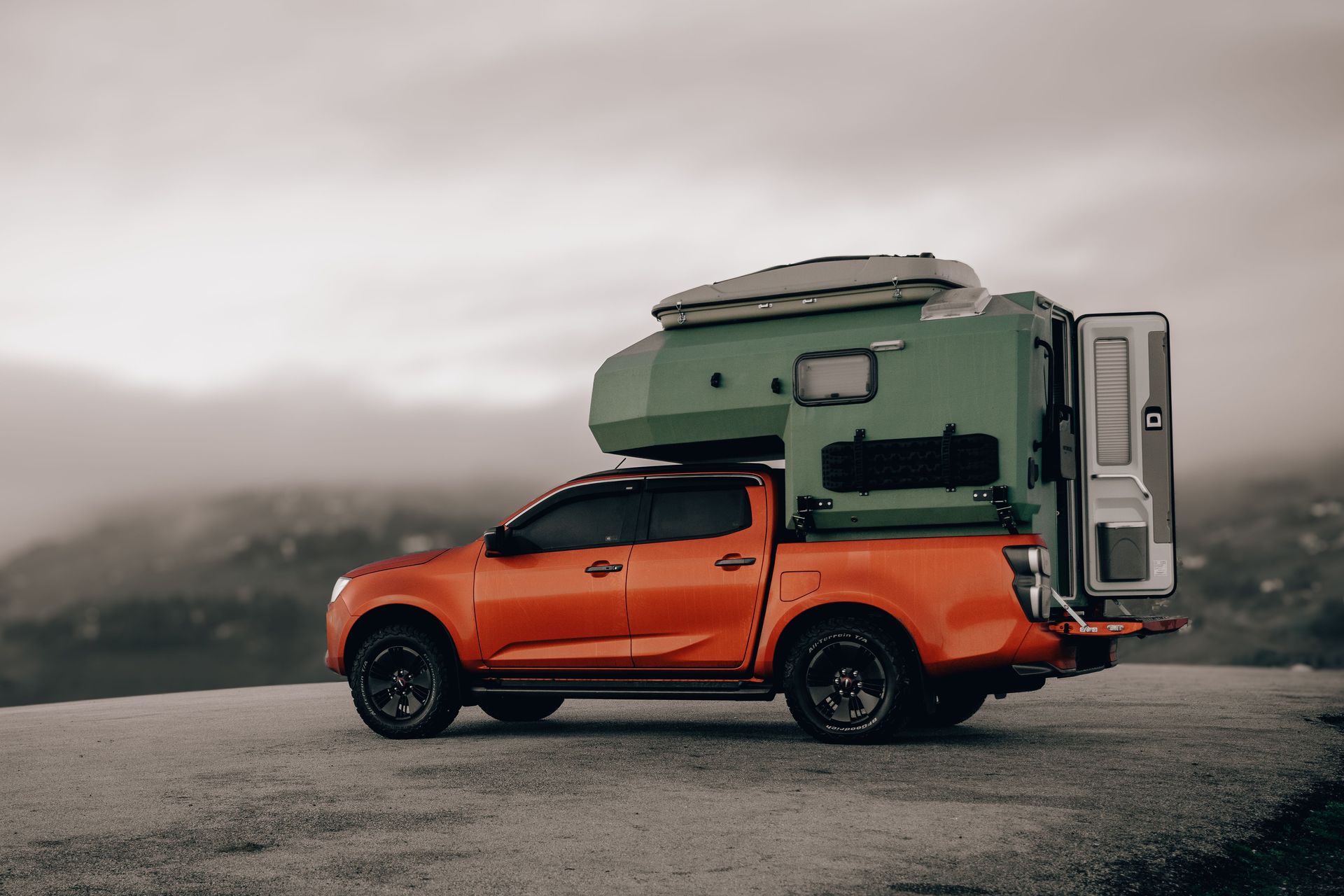 A vibrant orange pickup truck with a green camper stands on a mountain road in foggy Ordu, Türkiye.